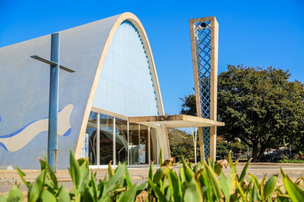 A modern curved concrete church with a tall lattice bell tower under a blue sky